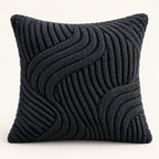 A square throw pillow in a dark charcoal gray color, featuring a textured, raised wavy pattern created by alternating thick and thin ribbed knit rows, set against a plain off-white background.