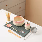 Ceramic matcha bowl set featuring a delicate cherry blossom design, complete with a bamboo whisk. The set showcases soft pink and white hues, perfect for 1