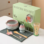 Ceramic matcha bowl set featuring a delicate cherry blossom design, complete with a bamboo whisk. The set showcases soft pink and white hues, perfect for 14