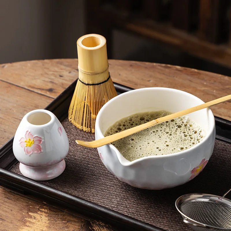 Elegant 5-piece ceramic matcha tea set featuring a delicate cherry blossom design. Includes a matcha bowl, whisk, scoop, and two cups. 1