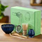 A set of traditional Japanese matcha tea preparation tools displayed in front of their packaging box, including a blue matcha bowl, a bamboo whisk, a bamboo rest, a metal sifting bowl, and two small blue cups.