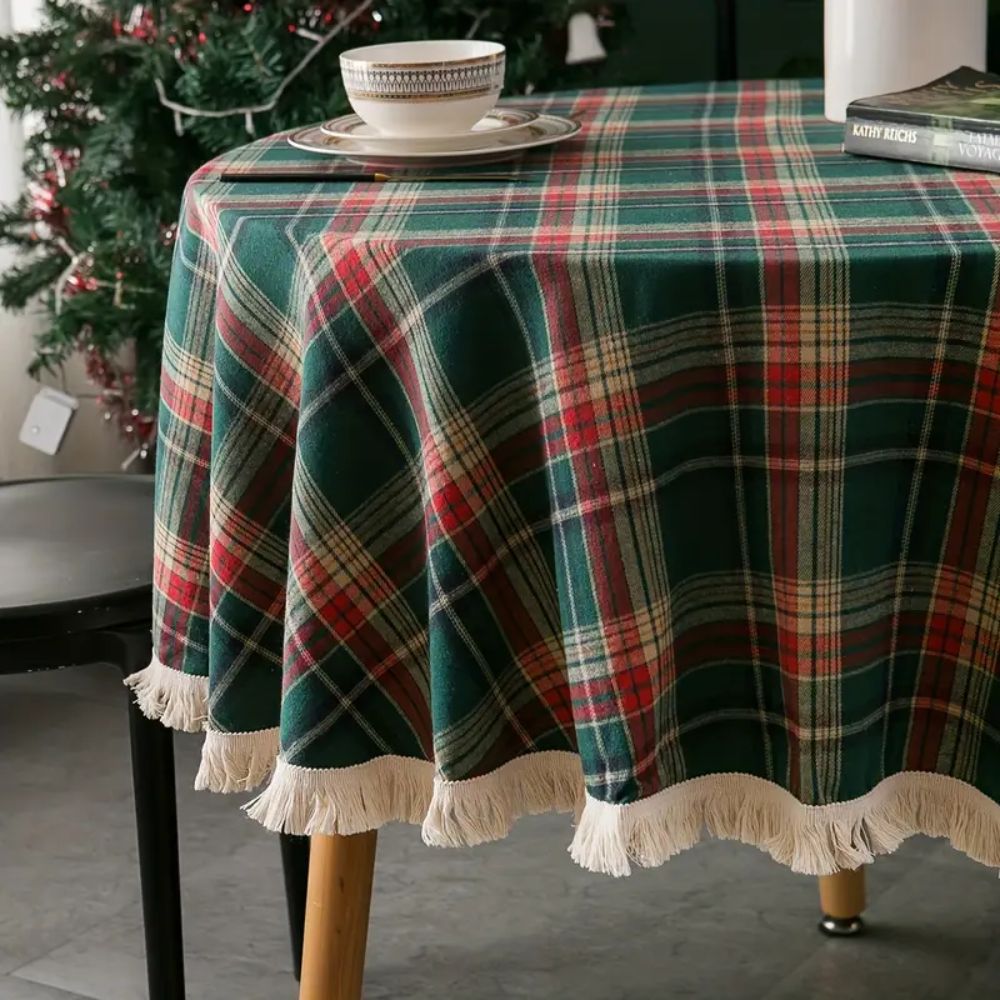 Round tablecloth featuring a vintage holiday plaid pattern in red, green, and white, adorned with decorative tassels. Made from durable fabric, perfect for 1