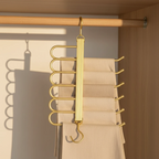 Gold multi-hook organizer hanging on a wooden rod with beige pants underneath.