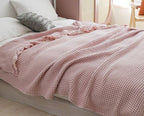 A pink waffle-weave blanket with ruffled edges draped over a bed in a softly lit bedroom setting.